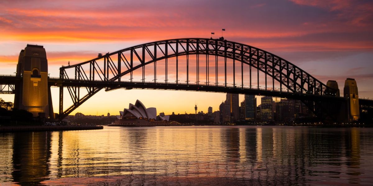 Which city is famous for its iconic harbor bridge, shown here at sunset